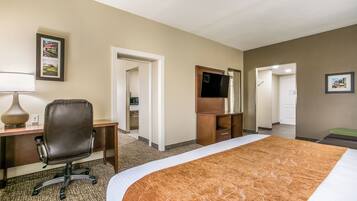 A hotel room with a bed, a desk, a chair, a dresser, a television, and a framed picture on the wall.