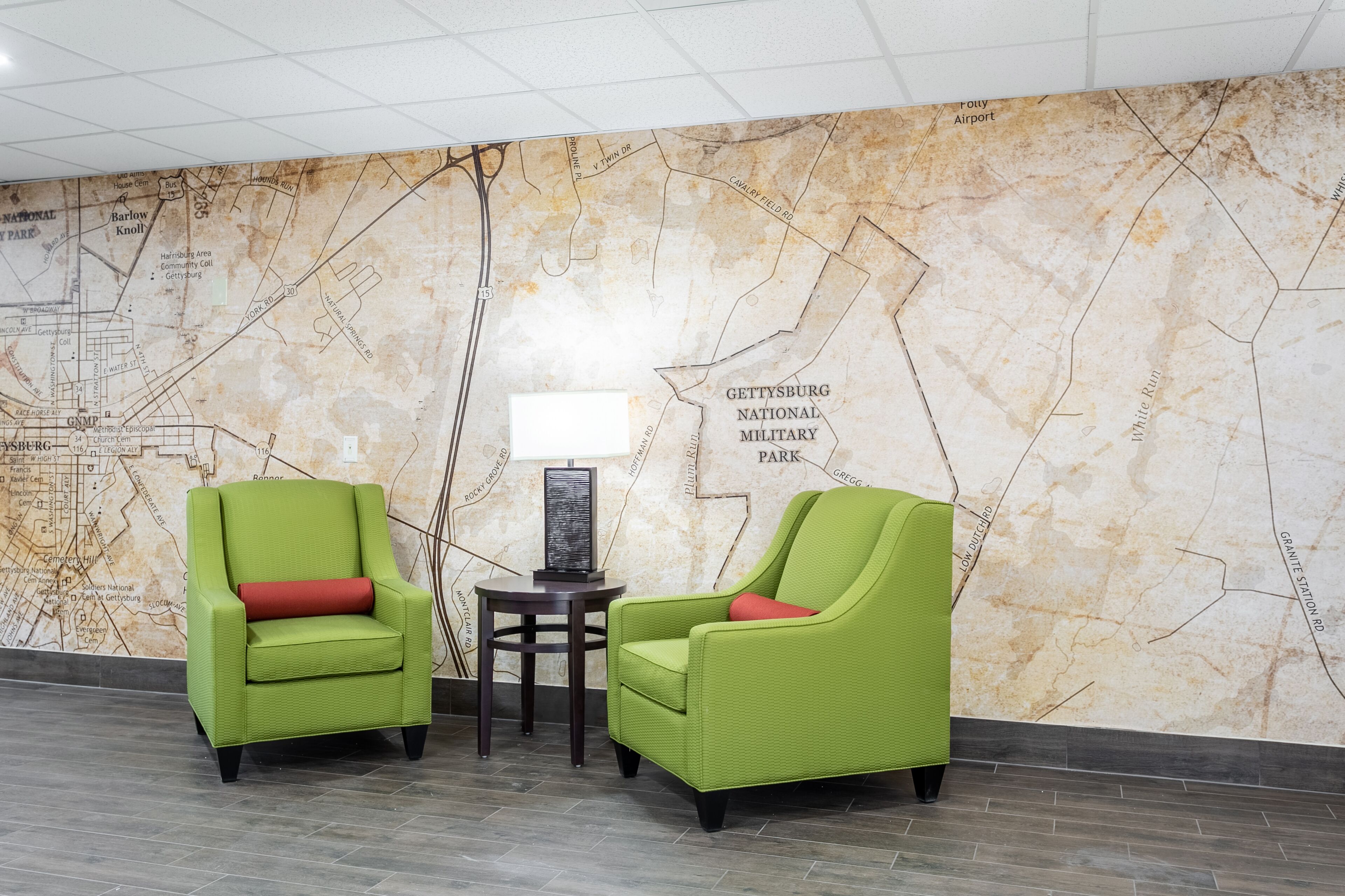 A lobby with two green armchairs, a small table with a lamp, and a map wall.