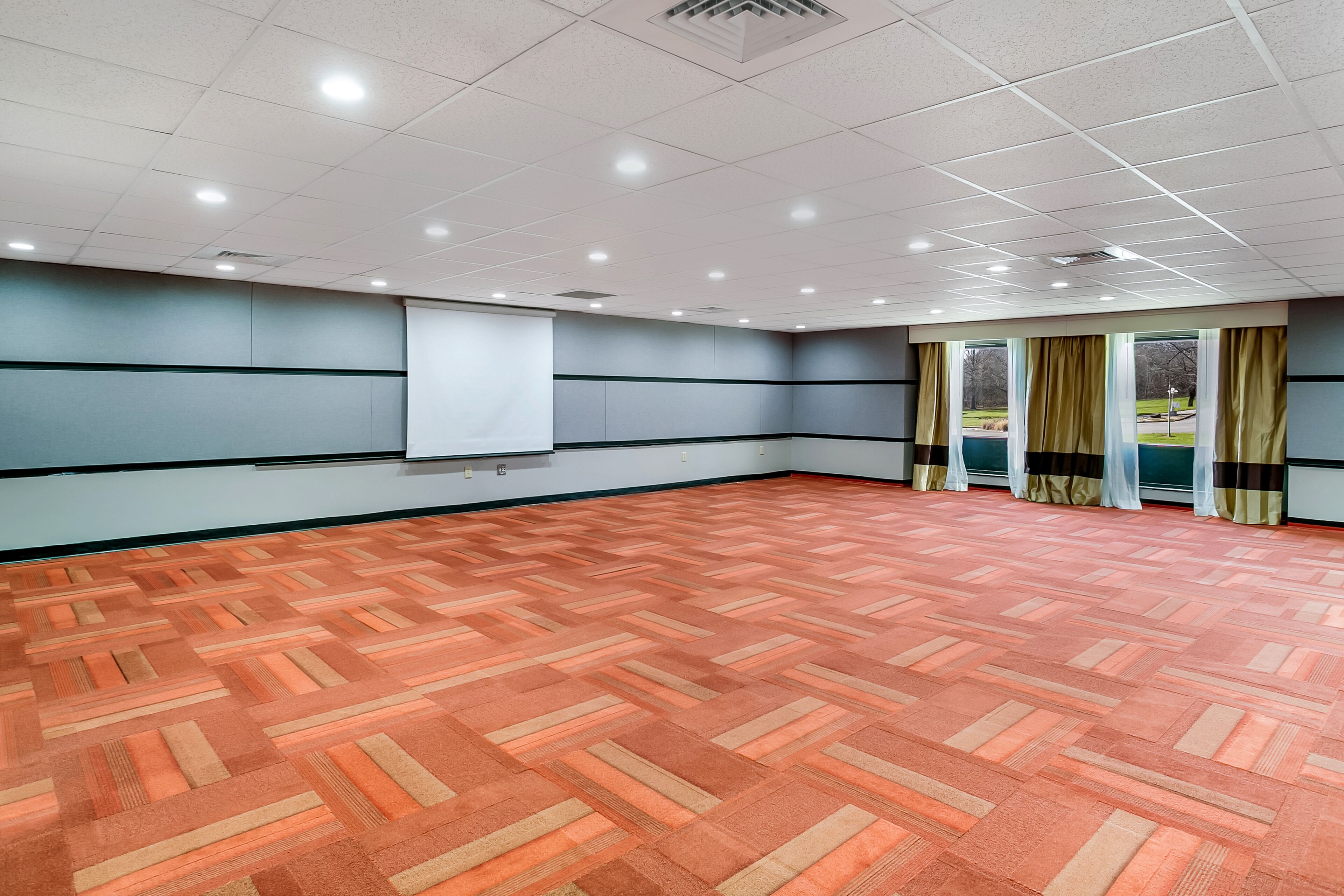 Un salón de conferencias con alfombra estampada, una pizarra y un ventanal con cortinas.