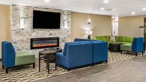 A lounge area with a stone wall, a flat-screen TV, a fireplace, and blue and green seating. - Aspire Gettysburg Hotel (Gettysburg)