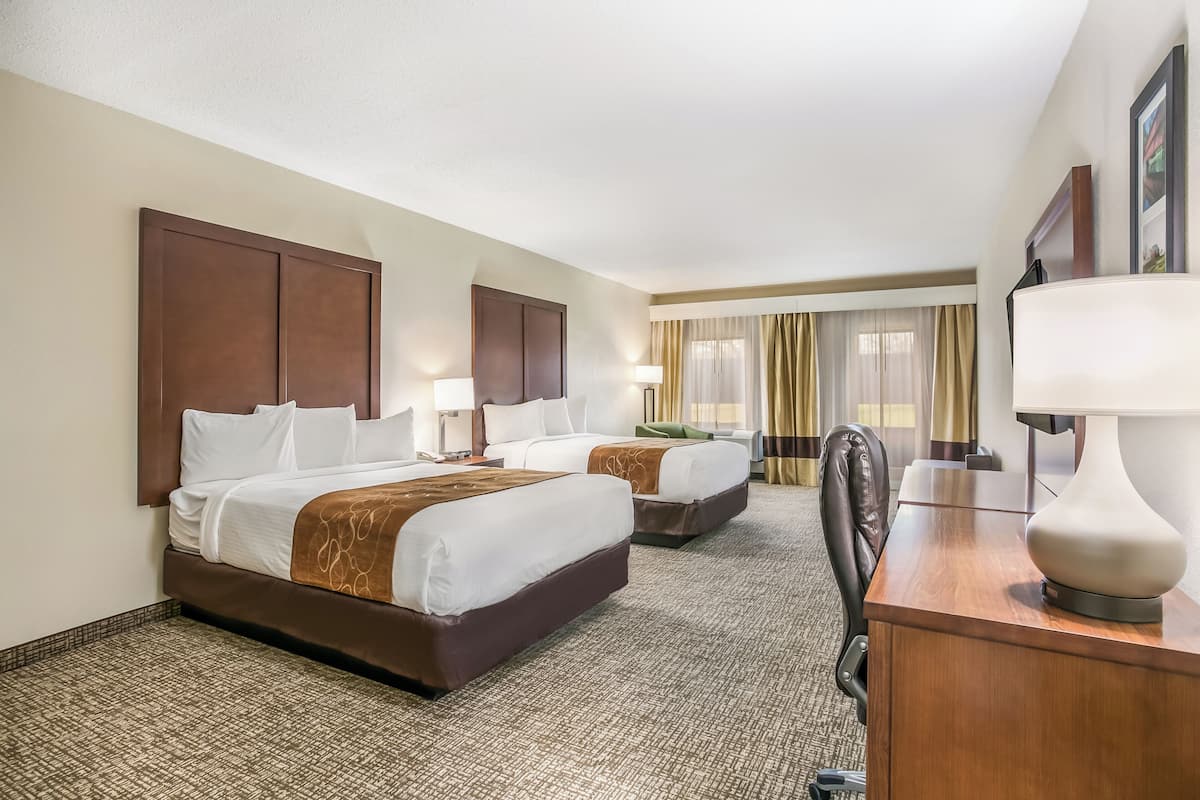 A hotel room with two beds, a desk, a chair, and a large window with curtains.