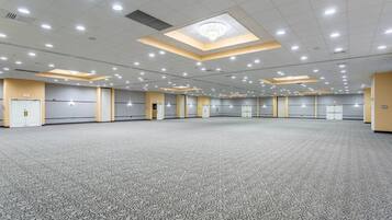 Een ruime, goed verlichte congreszaal met een kamerbreed tapijt, meerdere deuren, en een plafond met inbouwverlichting en een dakraam.