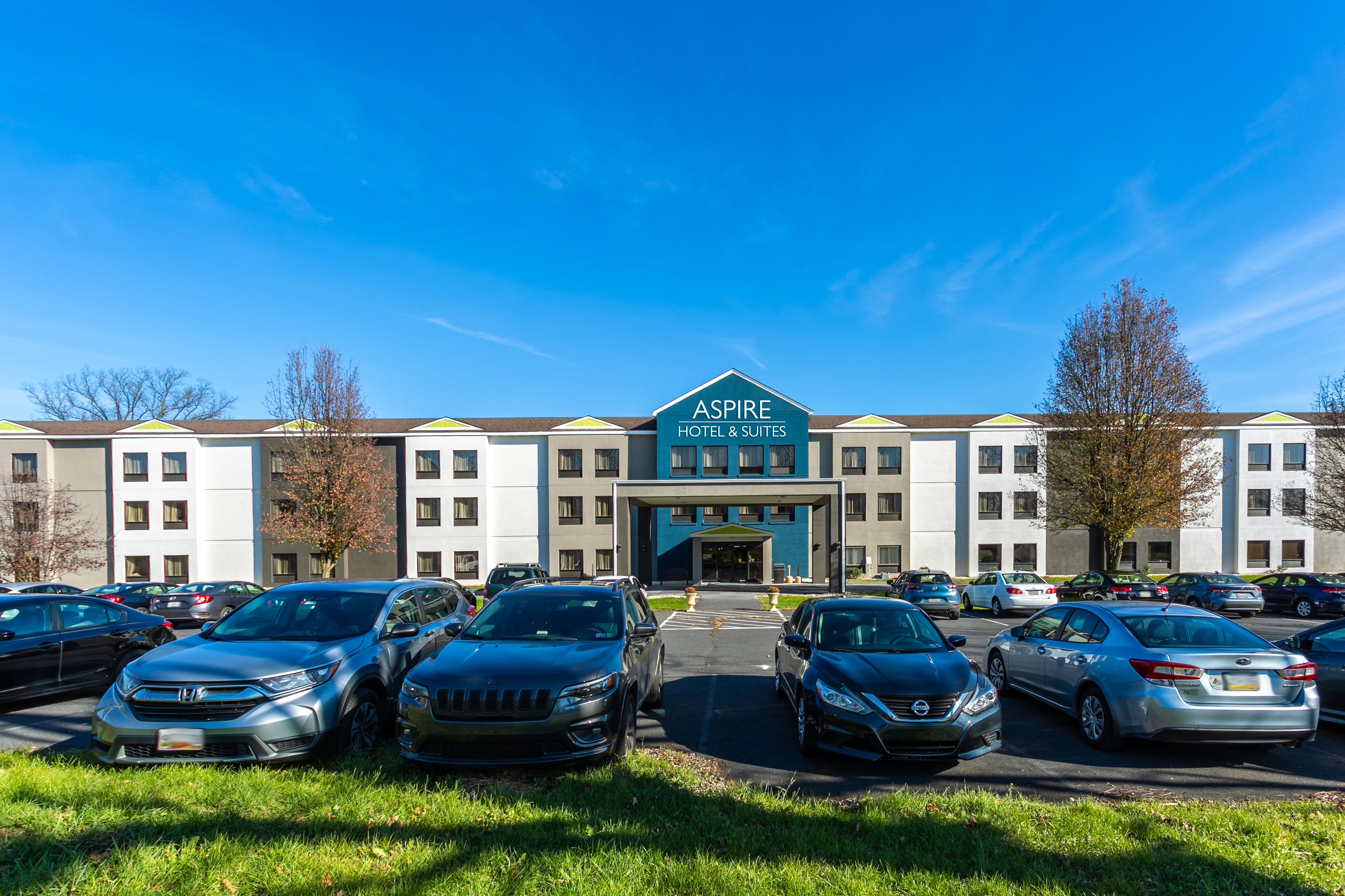 A hotel with a sign reading "Aspire Hotel & Suites" and a parking lot with several cars.