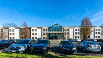 A hotel with a sign reading "Aspire Hotel & Suites" and a parking lot with several cars.