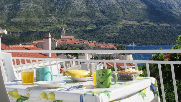 A balcony with a table set for breakfast, overlooking a mountainous landscape and a body of water. - Accommodation Drasko (Korcula)