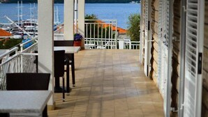 A covered outdoor area with a view of boats on a lake, a table, chairs, and a stone wall. - Accommodation Drasko (Korcula)