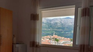 A room with a bed, a small refrigerator, and a window with a view of a mountainous landscape. - Accommodation Drasko (Korcula)