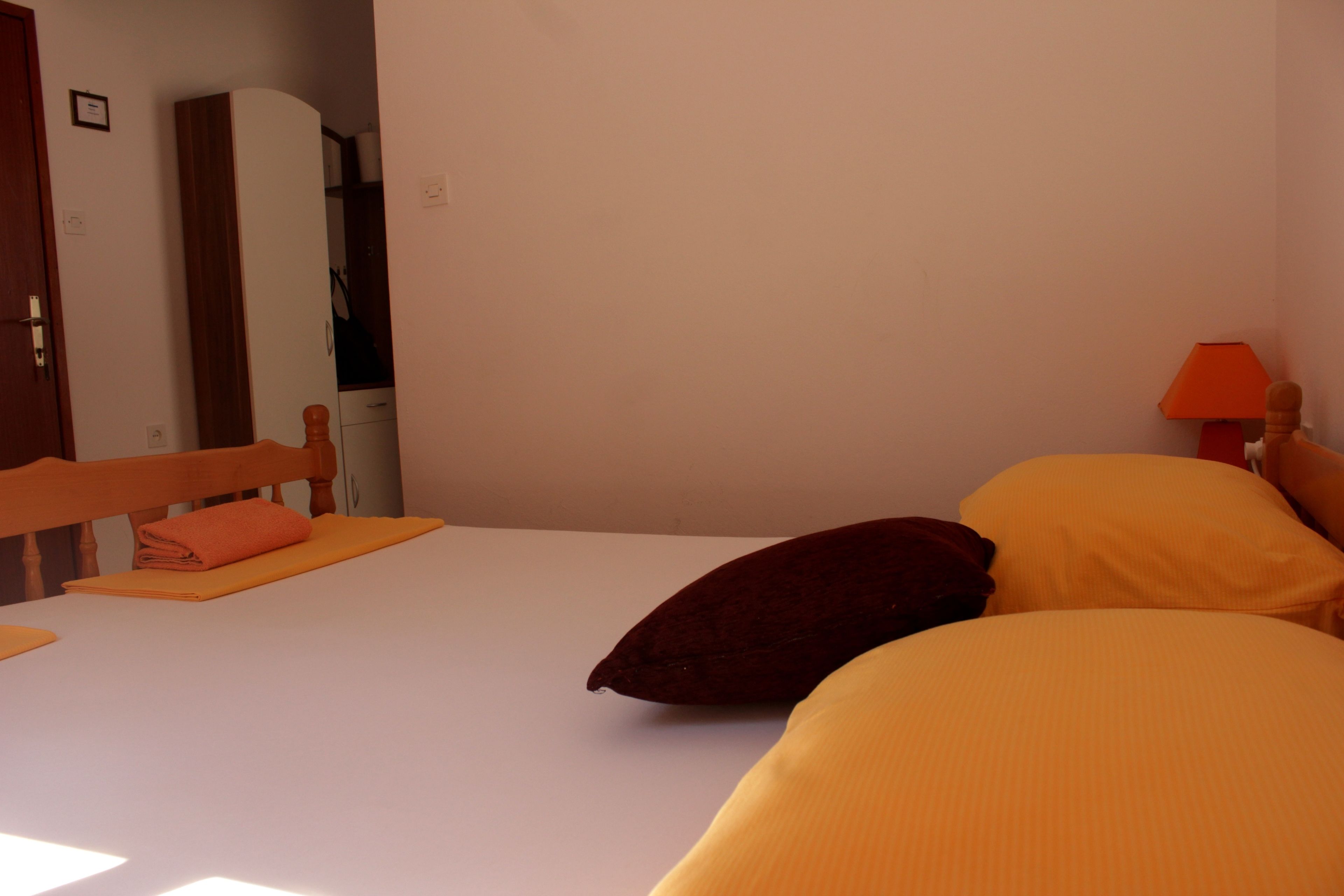 A bedroom with a bed, pillows, a nightstand, a lamp, and a wardrobe.