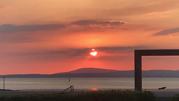 Un atardecer sobre una masa de agua, con el perfil de una cadena montañosa a lo lejos.