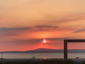 Un atardecer sobre una masa de agua, con el perfil de una cadena montañosa a lo lejos.
