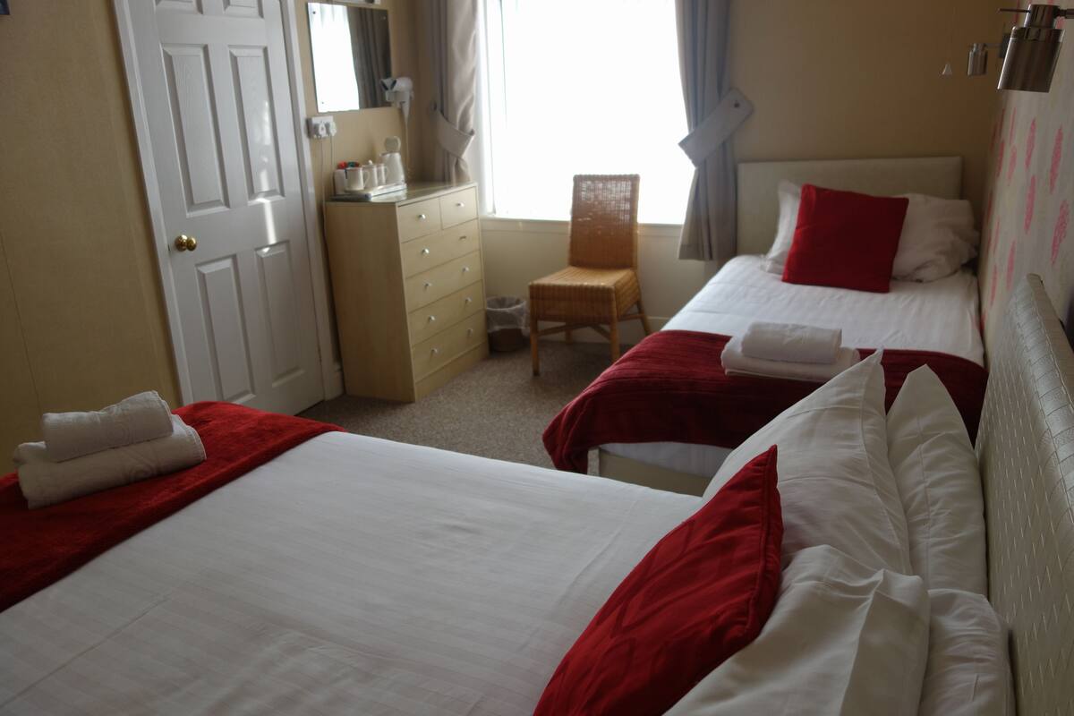 A hotel room with two beds, a dresser, a chair, and a window with curtains.