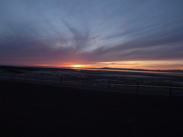 A sunset over a flat landscape with a fence in the foreground. - The Berkeley (Morecambe)