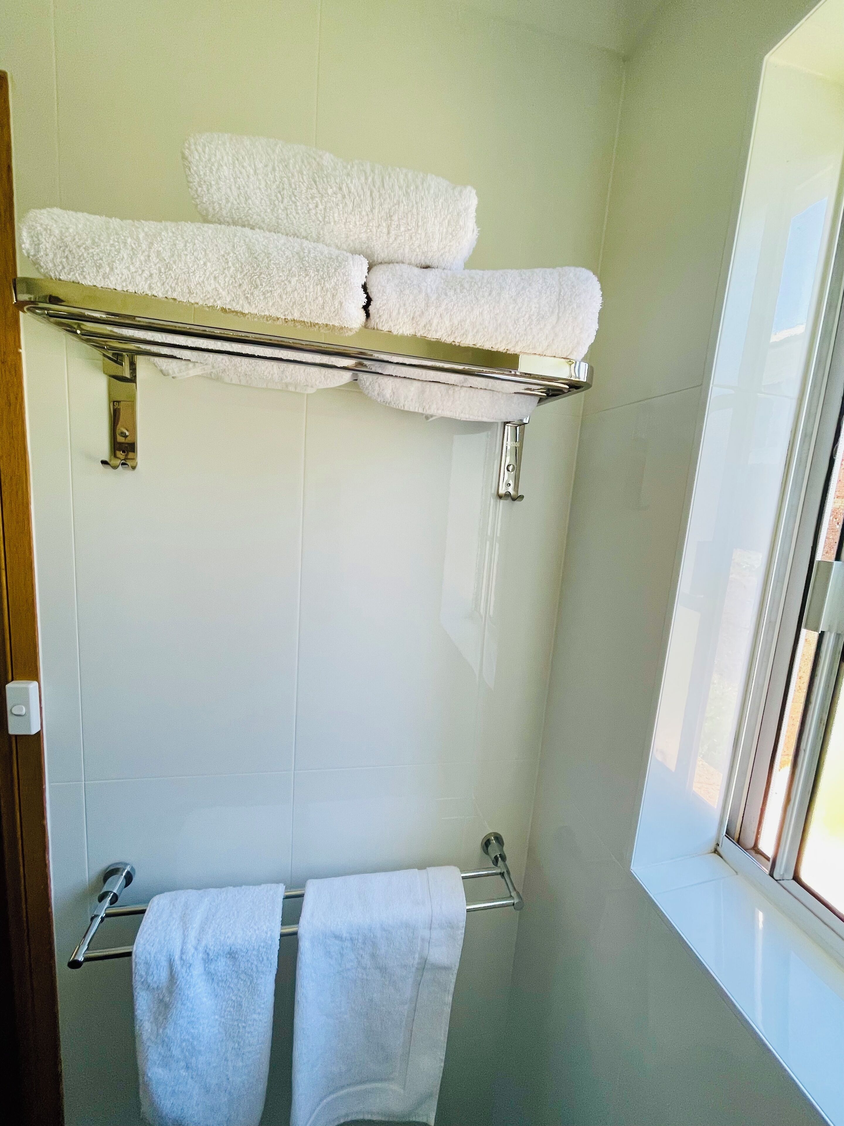 A bathroom with a towel rack, a towel rack with towels, and a window.