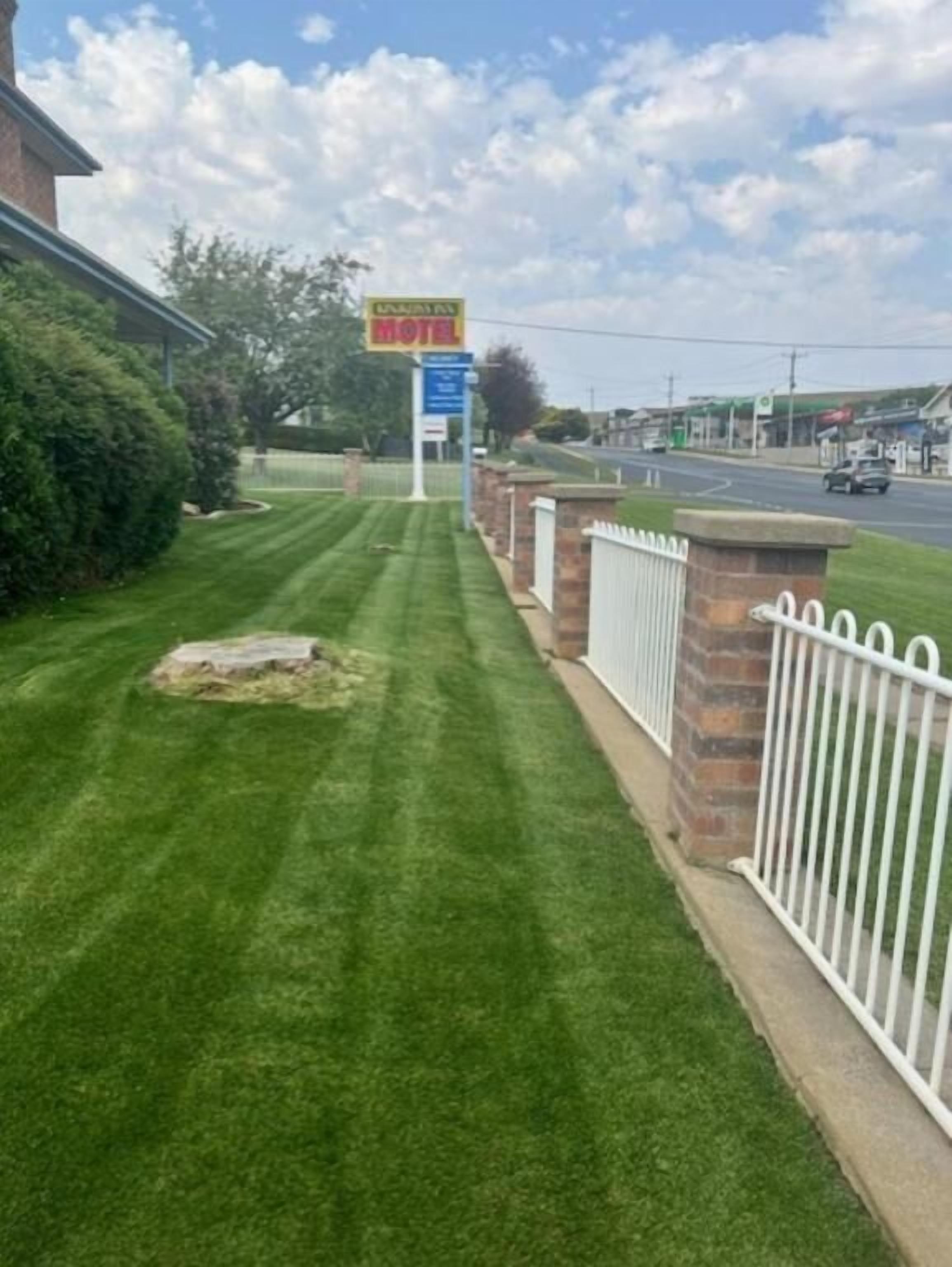 A hotel sign, a well-maintained lawn, and a white fence.