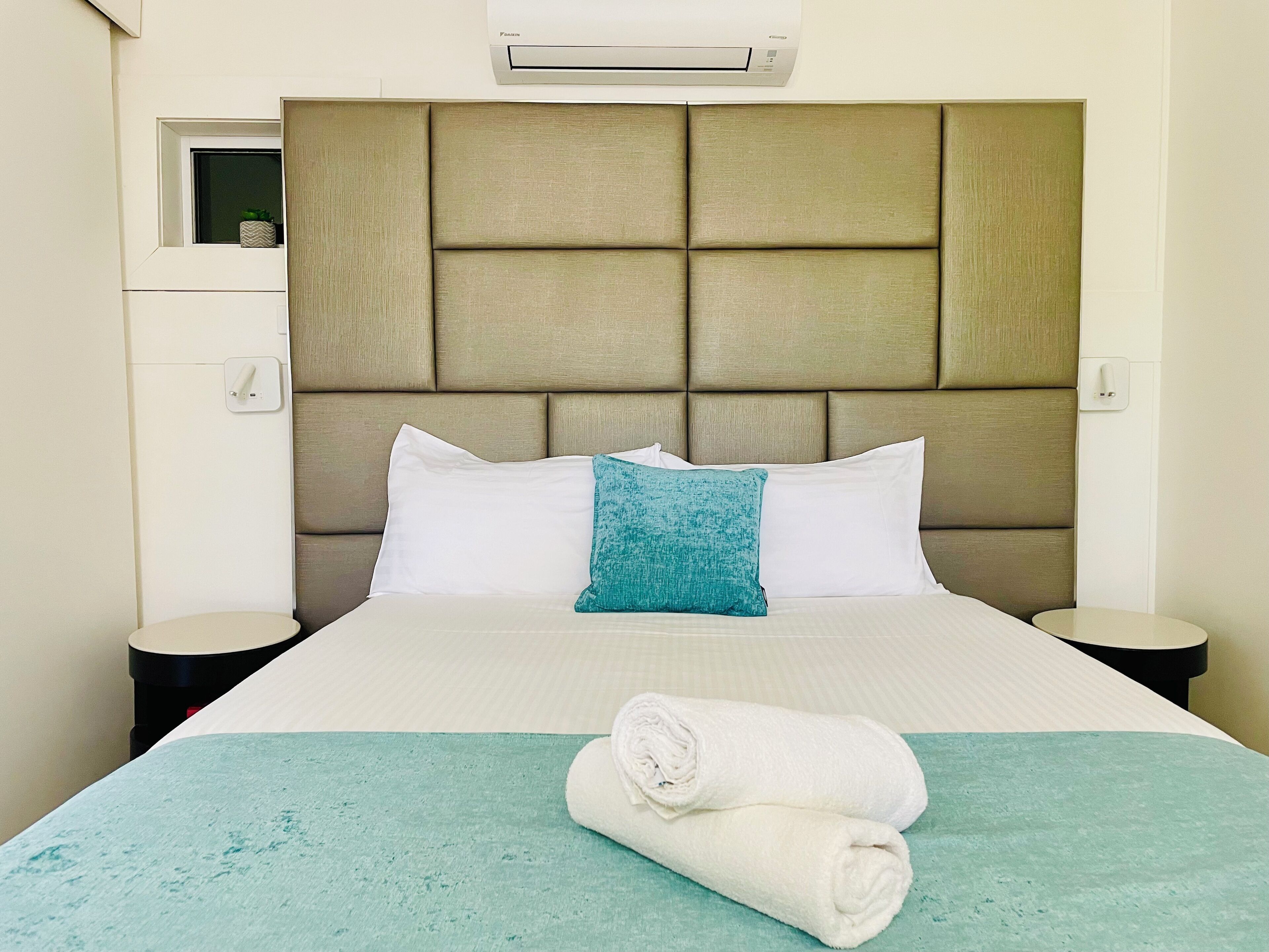 Una habitación de hotel con una cama grande, un cabecero, una ventana y un equipo de aire acondicionado.