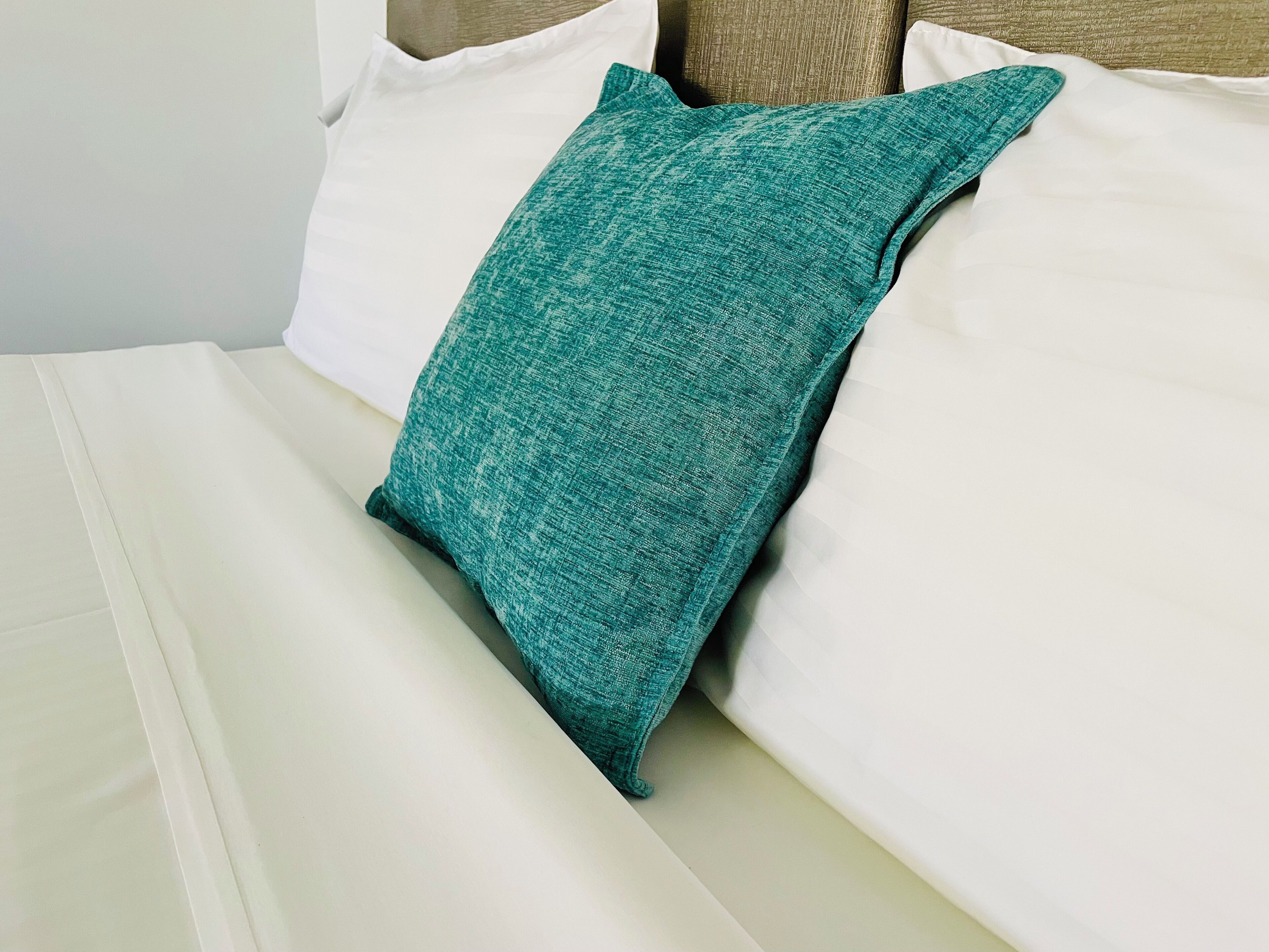 Ein Bett mit weißer Bettwäsche und einem türkisfarbenen Kopfkissen.