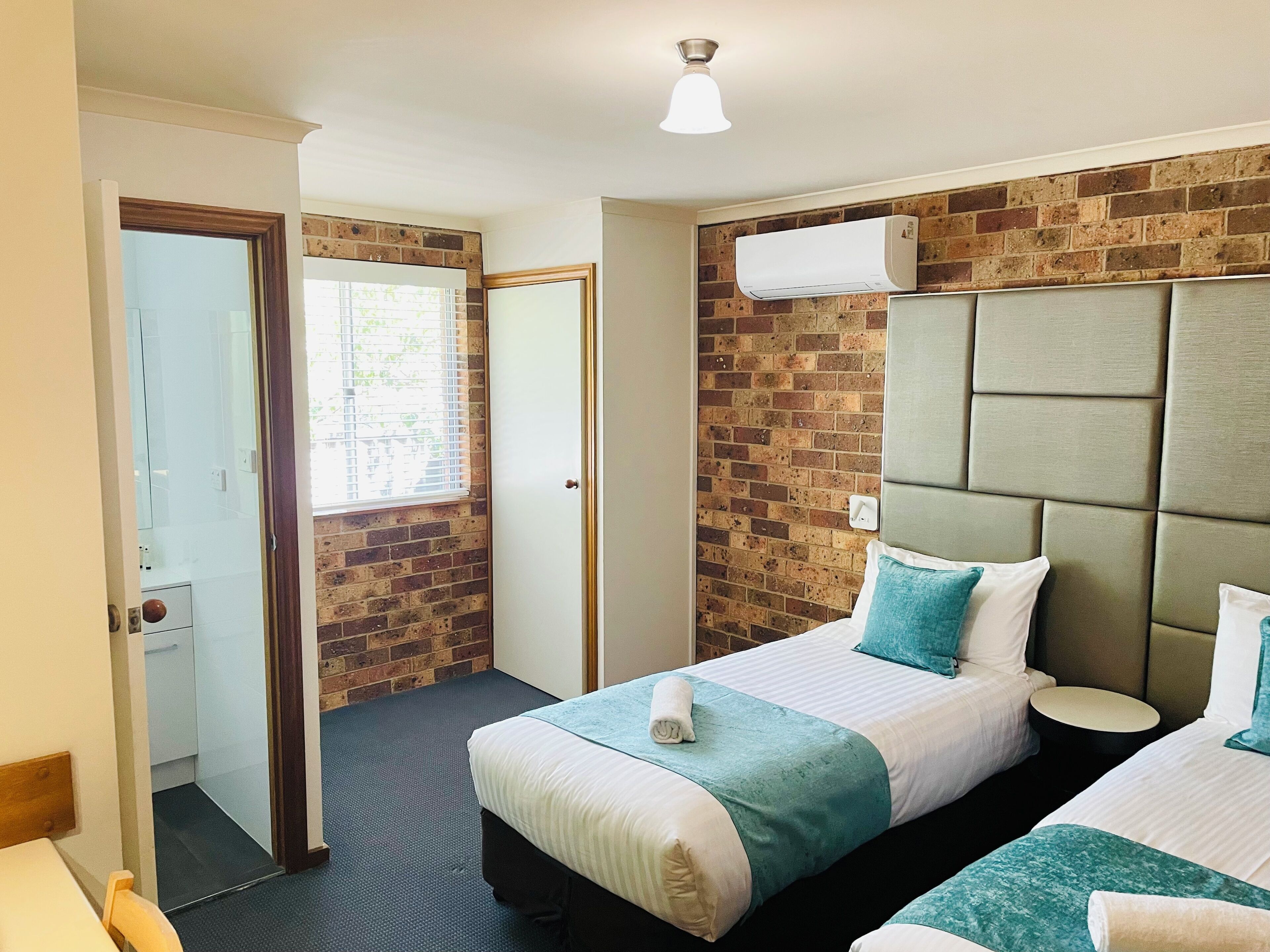 A hotel room with two beds, a brick wall, an air conditioning unit, and a small table.