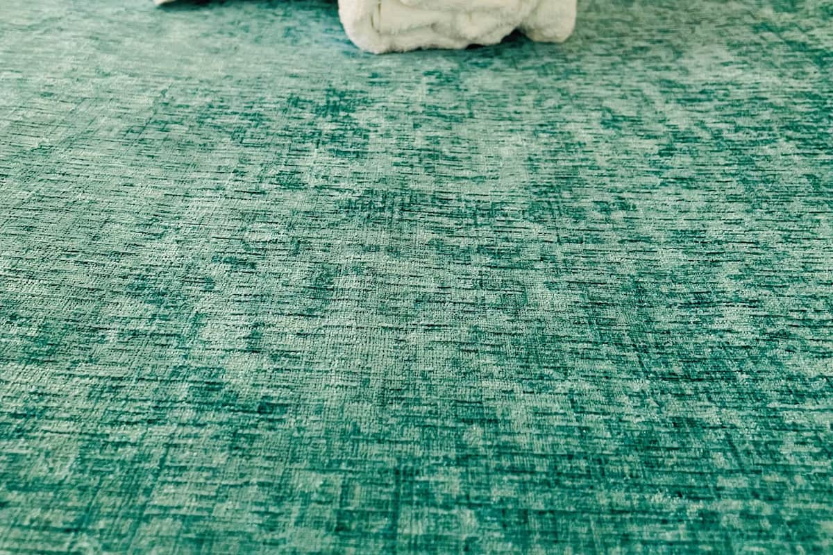 Una toalla blanca enrollada sobre una superficie texturizada color aguamarina, probablemente un tapete de baño o toallero.
