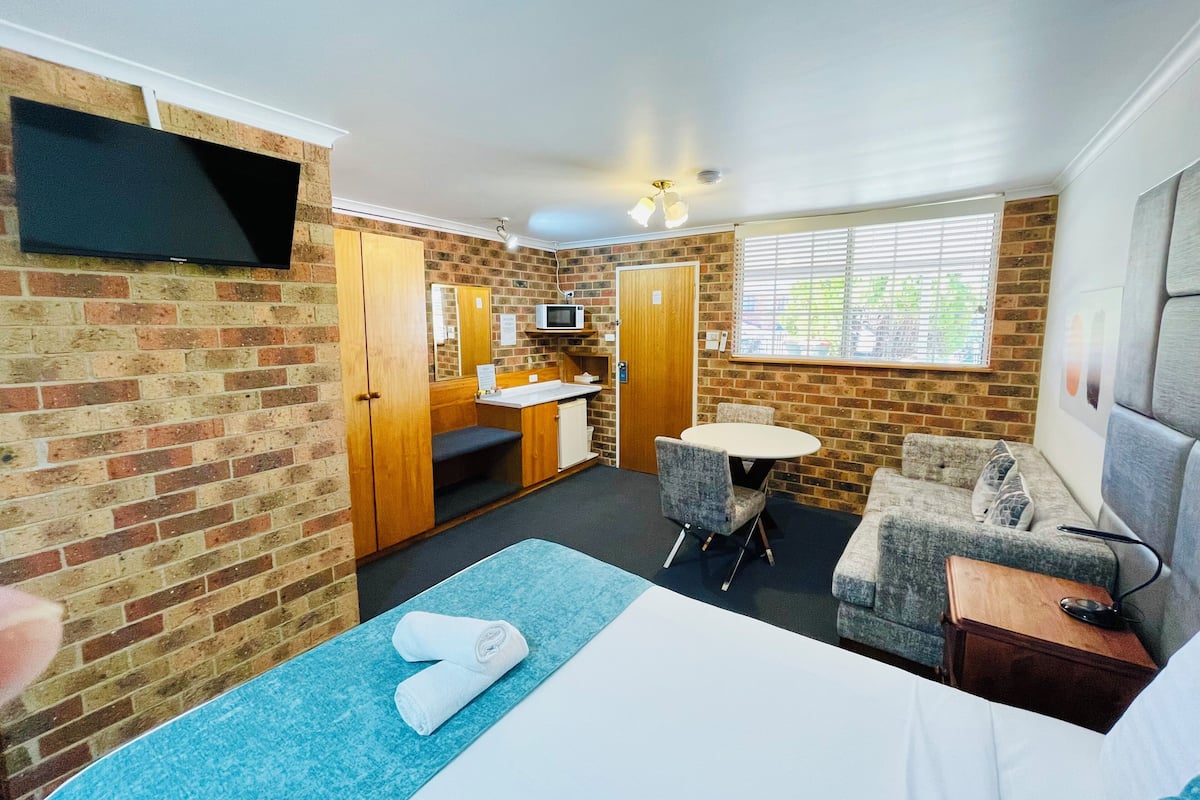 Habitación de hotel con cama, una kitchenette pequeña, un área de descanso con mesa y sillas, y un televisor montado en la pared.