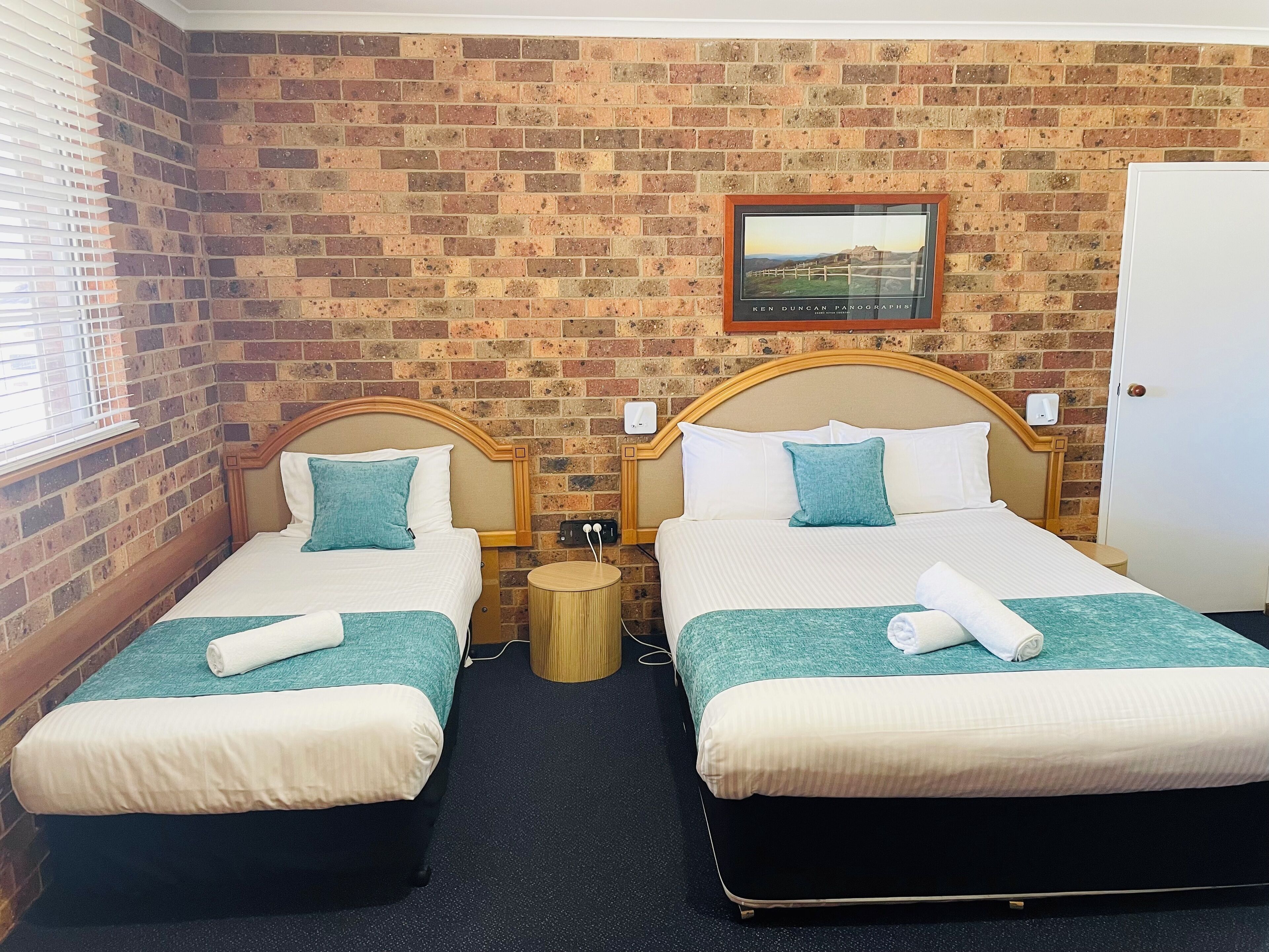 A hotel room with two beds, a brick wall, a framed picture, and a door.