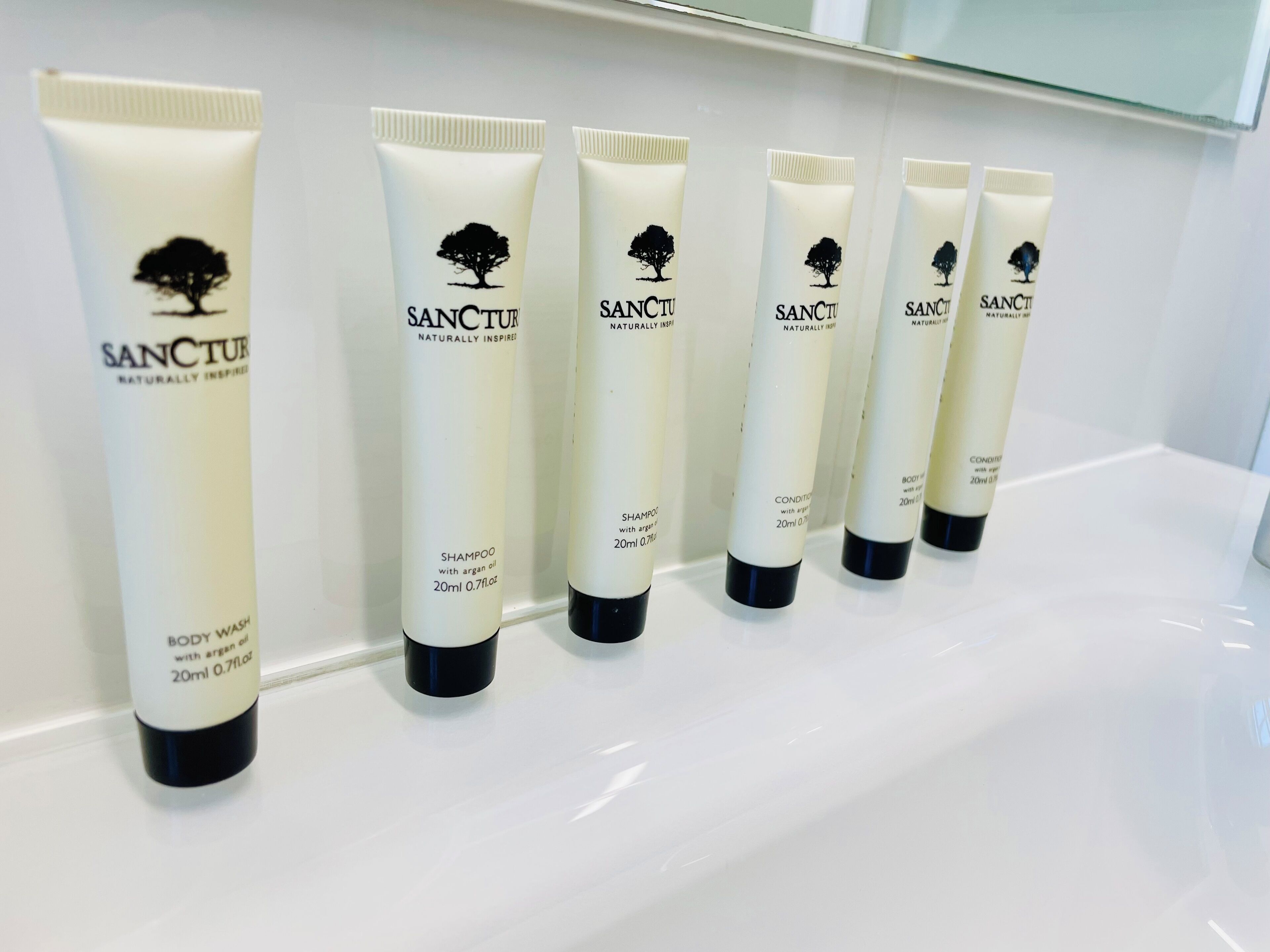 A row of six tubes of Sanctur body wash and shampoo on a white shelf.