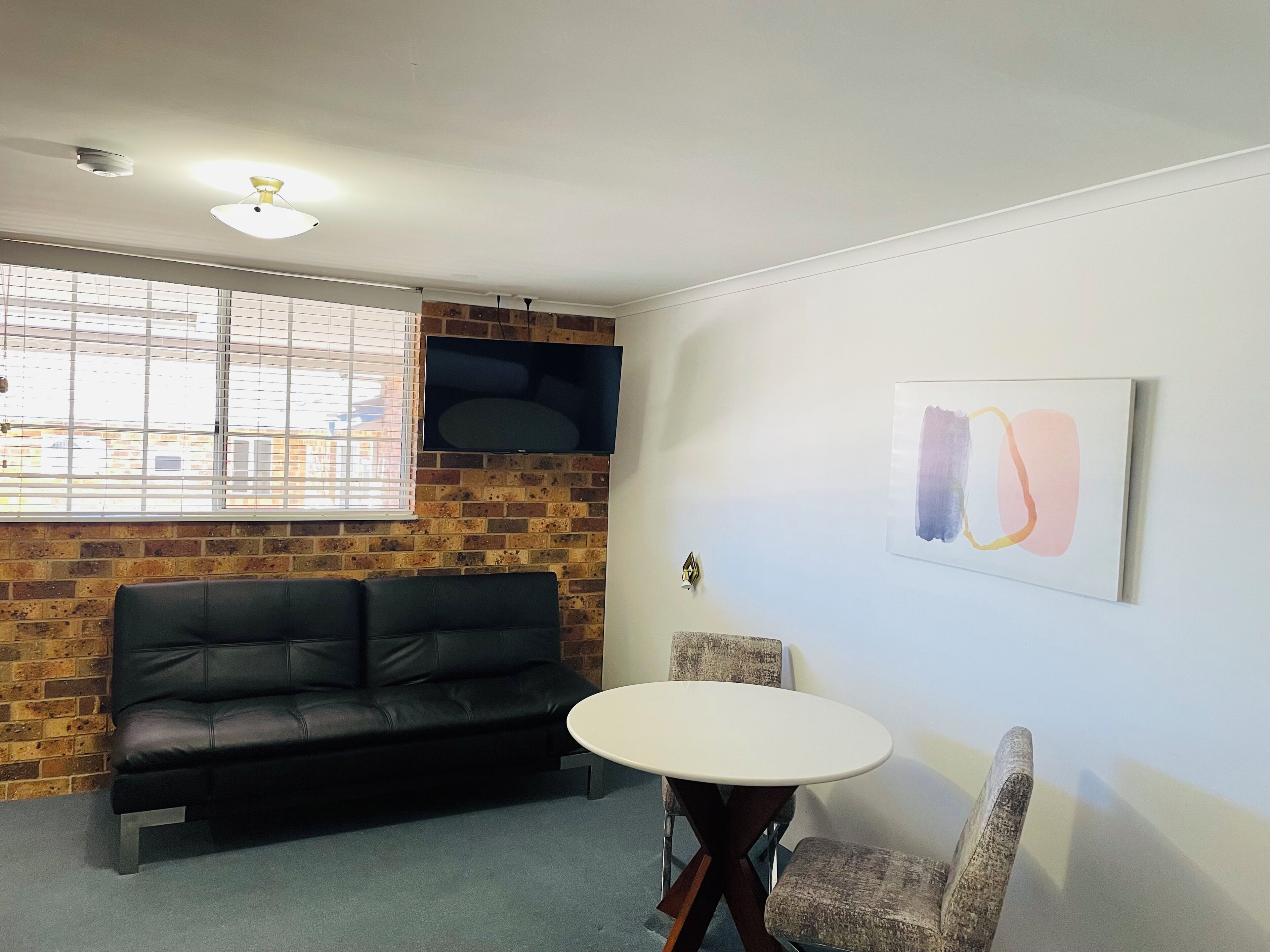 A room with a brick wall, a black leather couch, a round table, and two chairs.