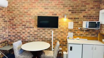 A room with a brick wall, a flat-screen TV, a microwave, a small refrigerator, and a round table with four chairs.
