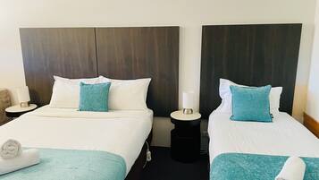 Two double beds with white linens and teal accents, a dark wood headboard, a small bedside table with a lamp, and a rolled towel on each bed.