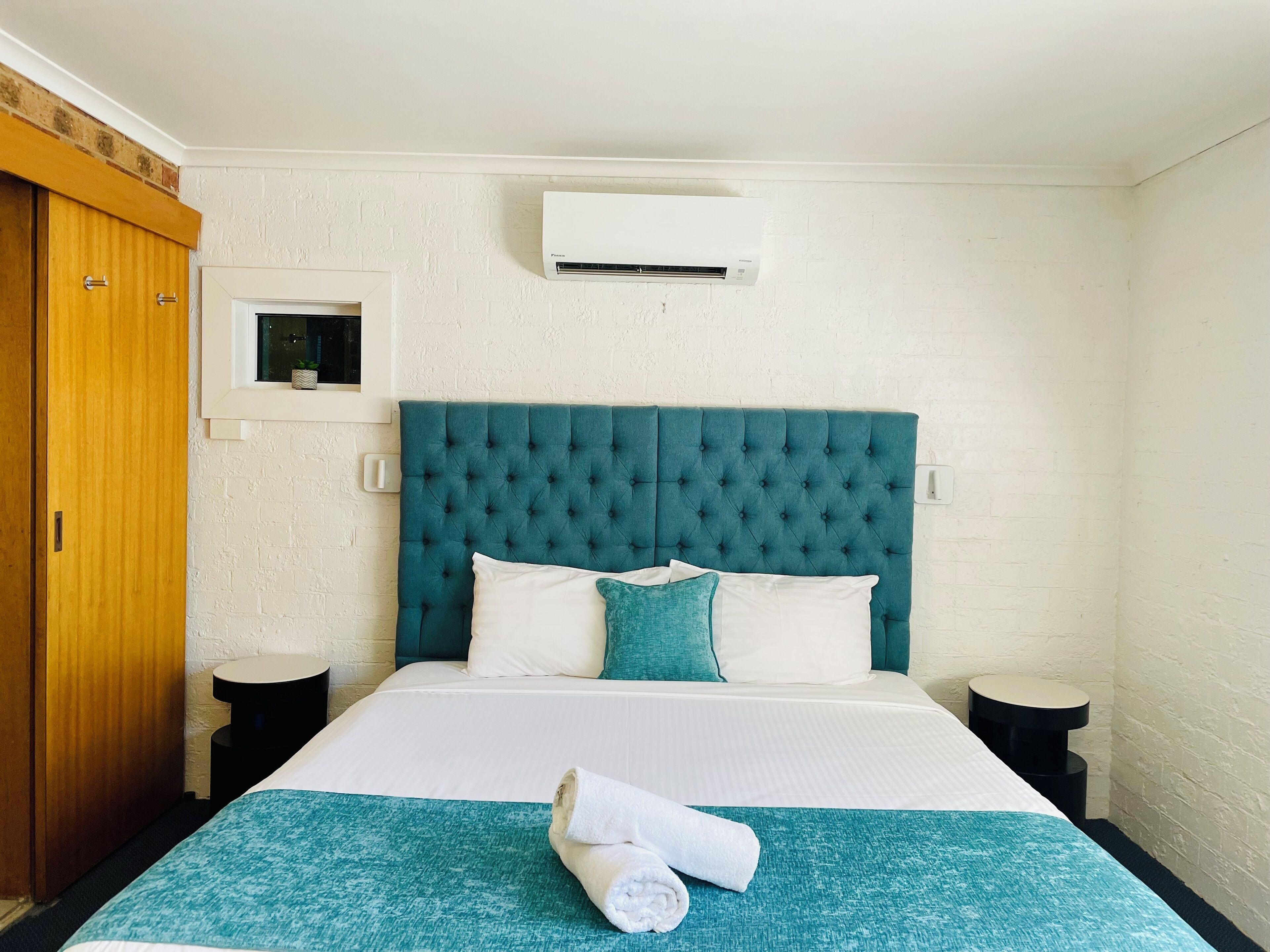 Quarto de hotel com cama, janela, guarda-roupa e ar condicionado.
