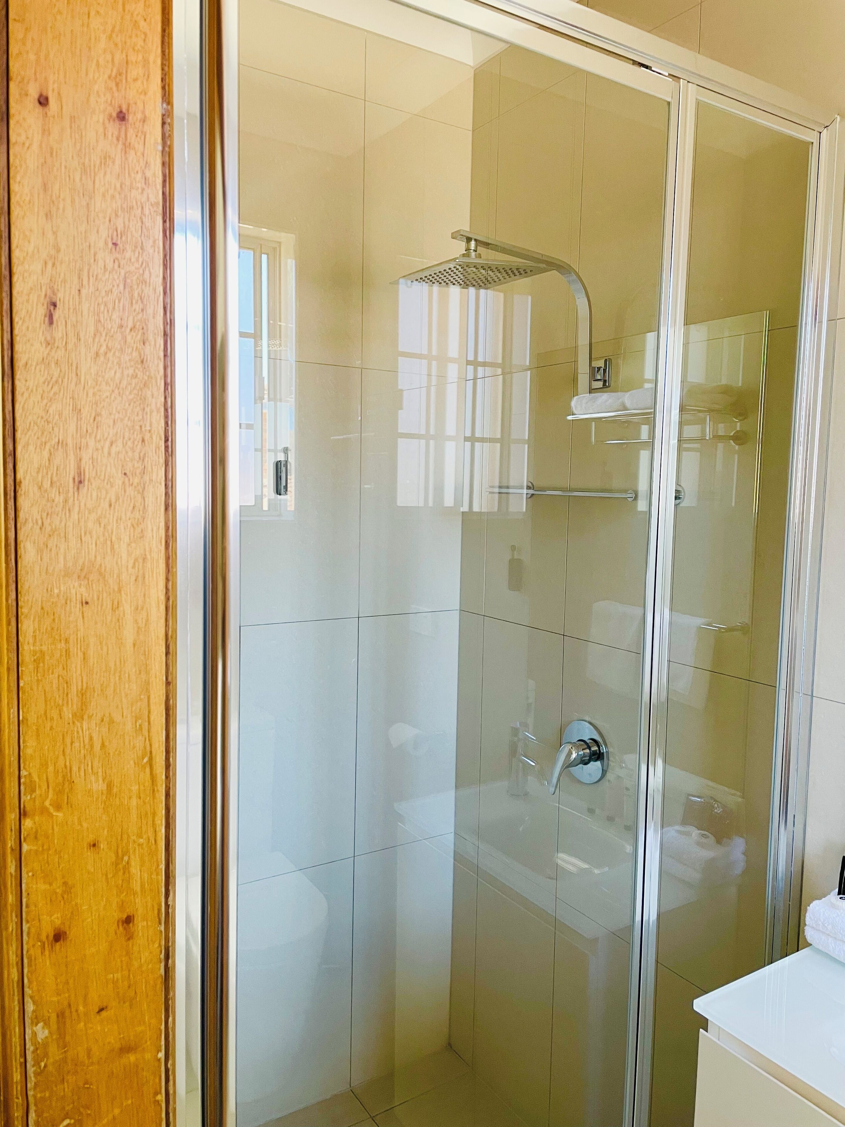 Une salle de bain moderne avec une douche à parois de verre, un lavabo blanc et un cadre de porte en bois.