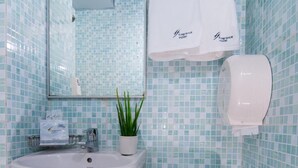 A bathroom with a sink, toilet, and a mirror. There are towels hanging on the wall and a plant on the sink.