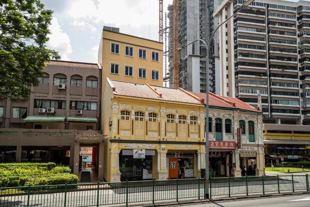 A yellow building with a red roof, a sign for a hotel, and a construction crane in the background.