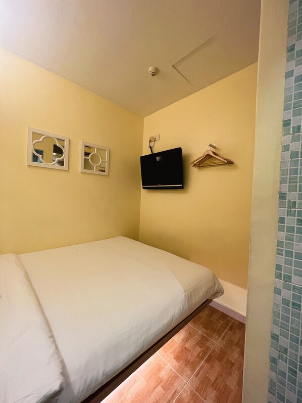 A small, single-bed room with a plain bed, a mounted TV, and a wall-mounted coat rack.