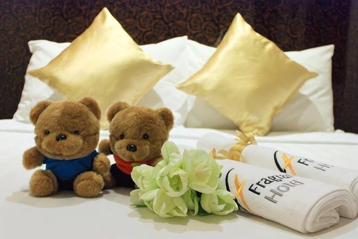 Deux ours en peluche sur un lit, avec des oreillers dorés et un bouquet de fleurs.