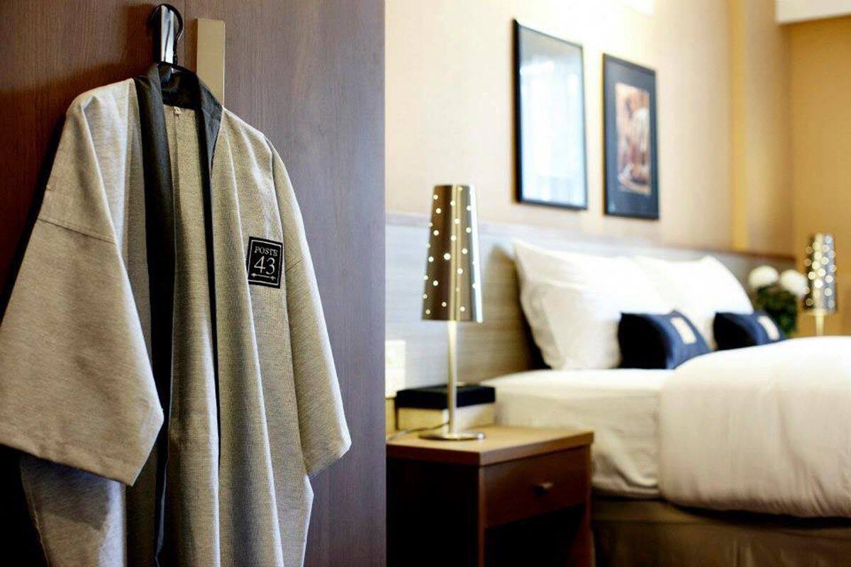 A hotel room with a bed, a nightstand, a lamp, and a coat hanging on a rack.