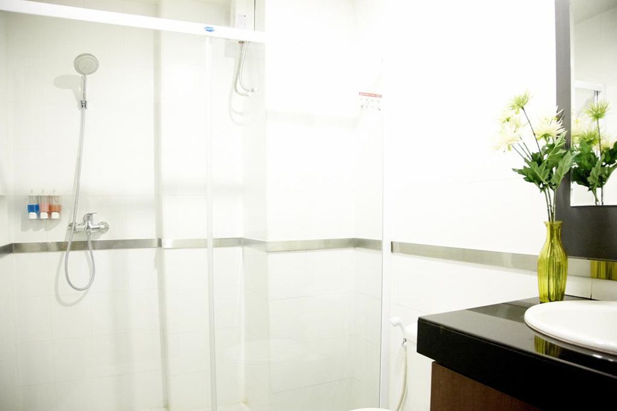 A bathroom with a glass-enclosed shower, a sink with a mirror, and a vase with flowers on the counter.