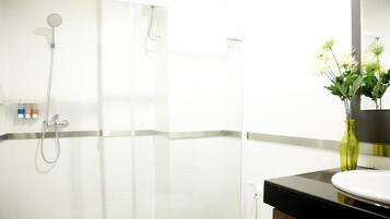 A bathroom with a glass-enclosed shower, a sink with a mirror, and a vase with flowers on the counter.