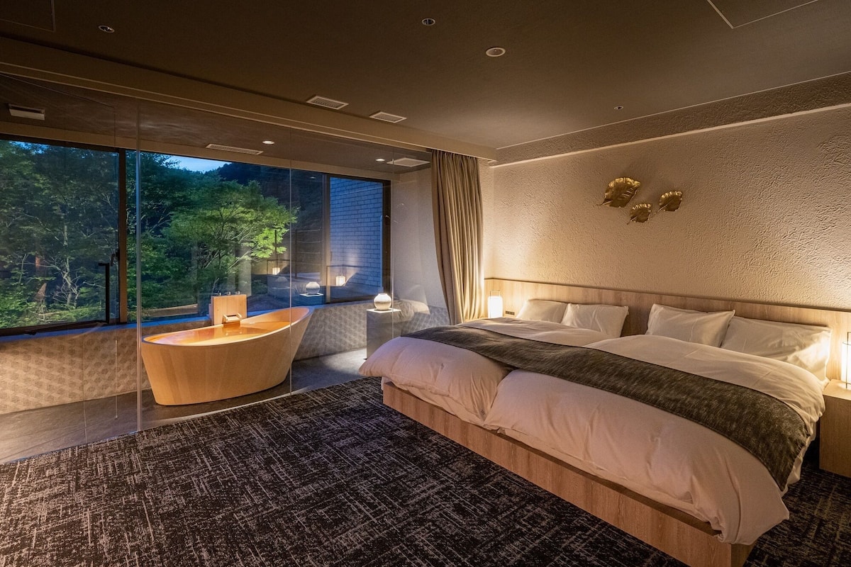 A modern bedroom with a large bed, a seating area, and a view of the outdoors.
