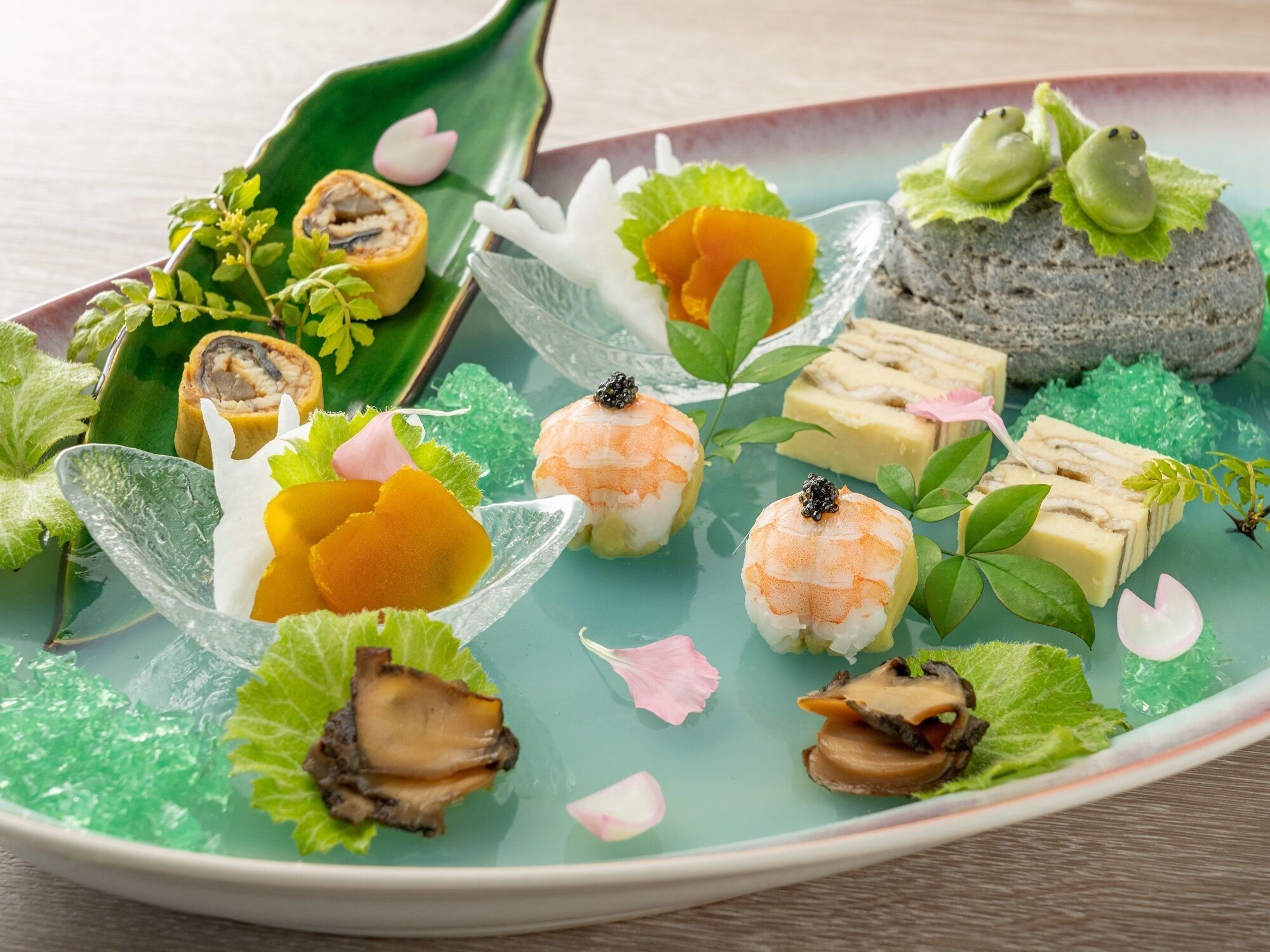 Diversos tipos de sushi e sashimi dispostos numa placa verde em formato de folha, decorada com flores e folhas.