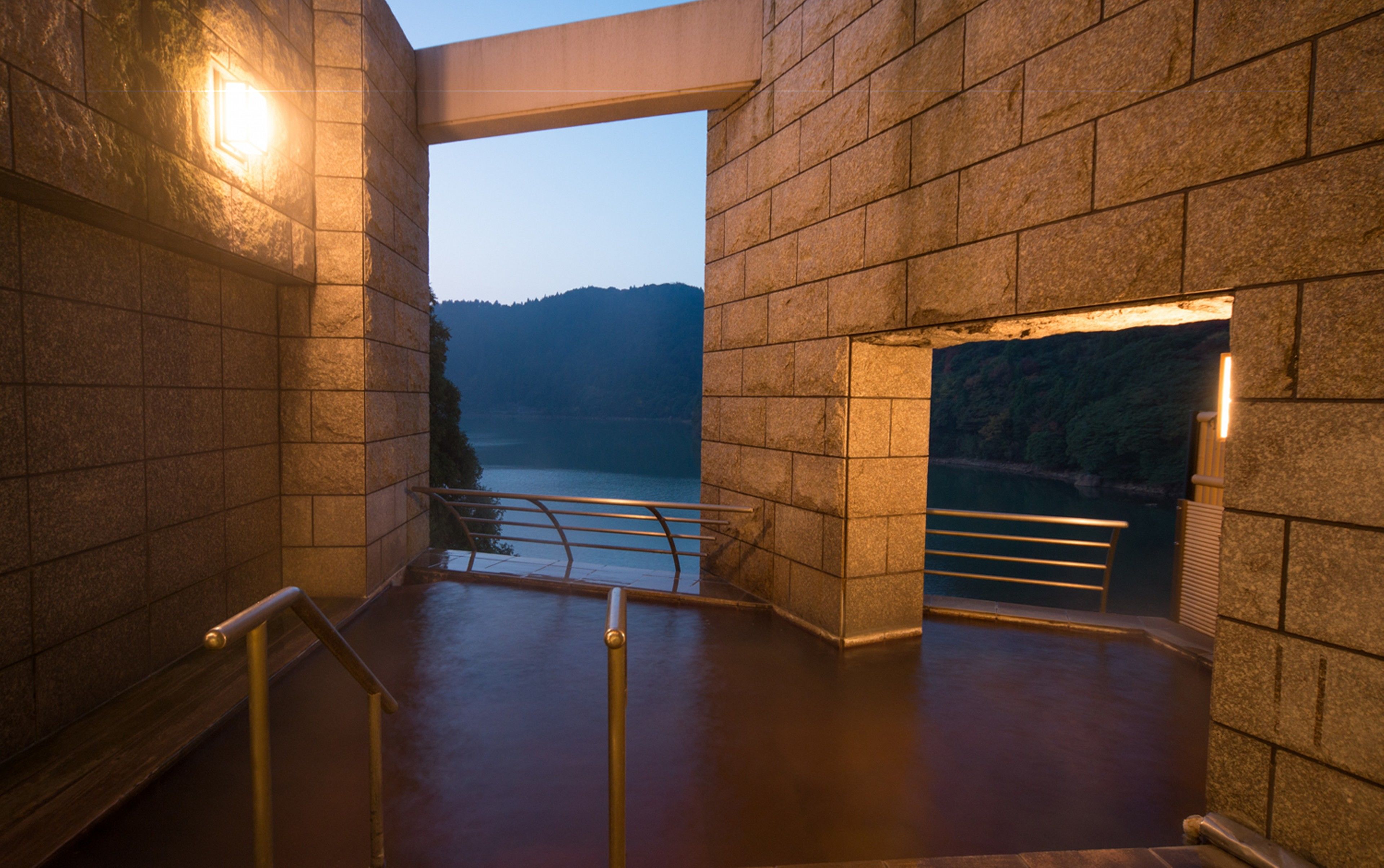 A stone staircase leading to a terrace with a view of a body of water and hills.