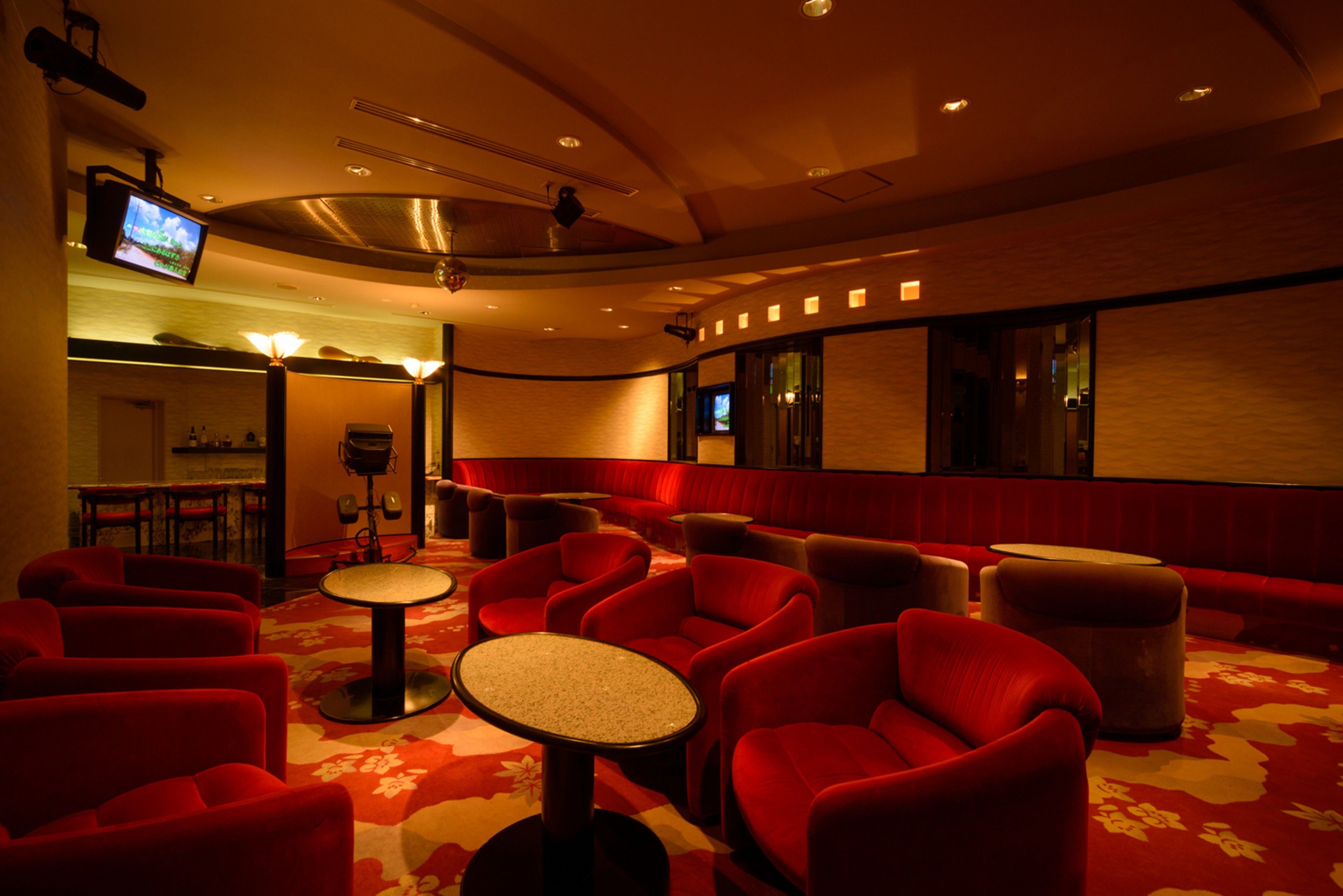 A hotel lobby with red seating, a small round table, and a television mounted on the wall.