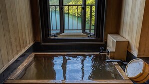 Une baignoire en bois offrant une vue sur un lac et une forêt, grâce à une grande fenêtre.
