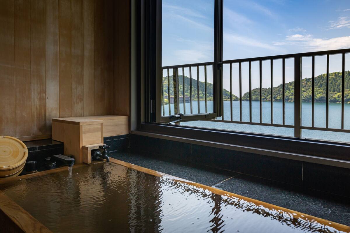 A wooden bath with a view of a lake and hills.