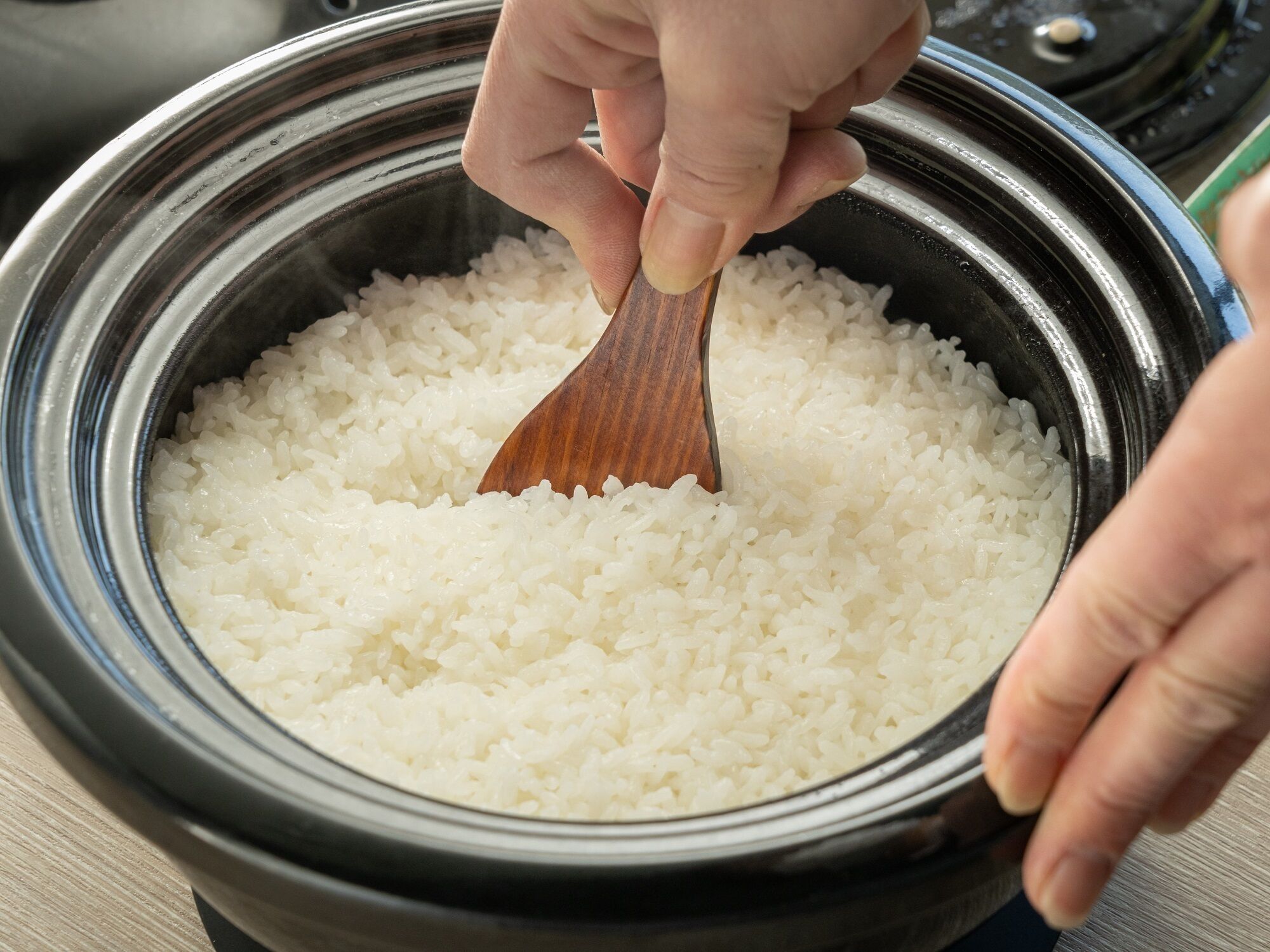A hand stirring white rice in a black pot.