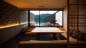 Un intérieur moderne avec un mur en pierre, une grande fenêtre donnant sur un lac et un coin salon avec une table et des chaises.