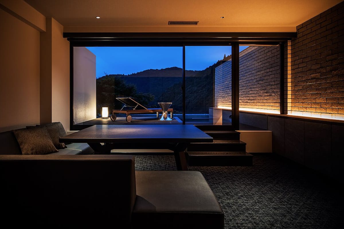 A modern interior with a dining area, a sofa, and a view of a mountainous landscape through large windows.
