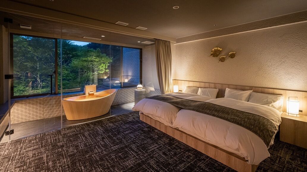 A modern bedroom with a large bed, a round seating area, and a view of the outdoors.