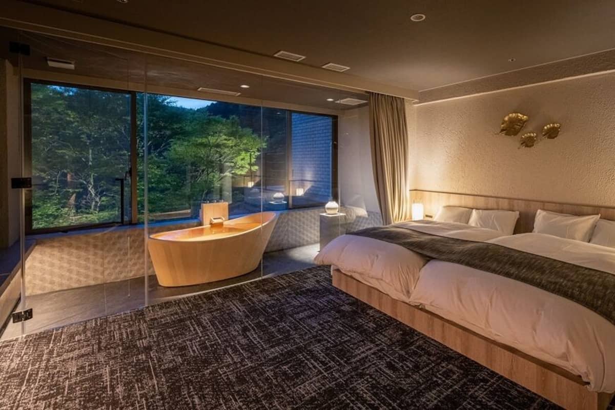 A modern bedroom with a large bed, a round seating area, and a view of the outdoors.