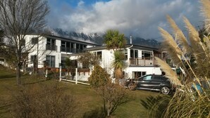 Una casa moderna de dos pisos amb un balcó, envoltada de muntanyes i arbres.