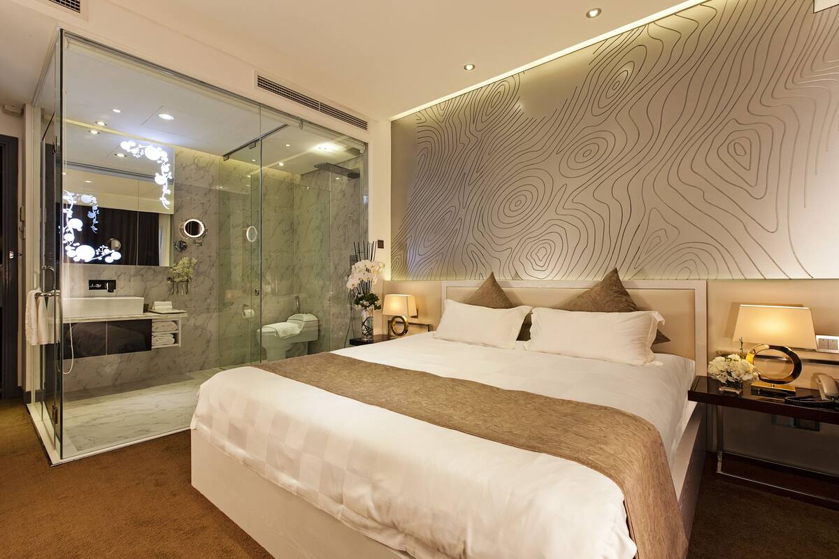 Una habitación de hotel moderna con una cama grande, cabina de ducha con paredes de vidrio, baño de mármol y un diseño de pared original.